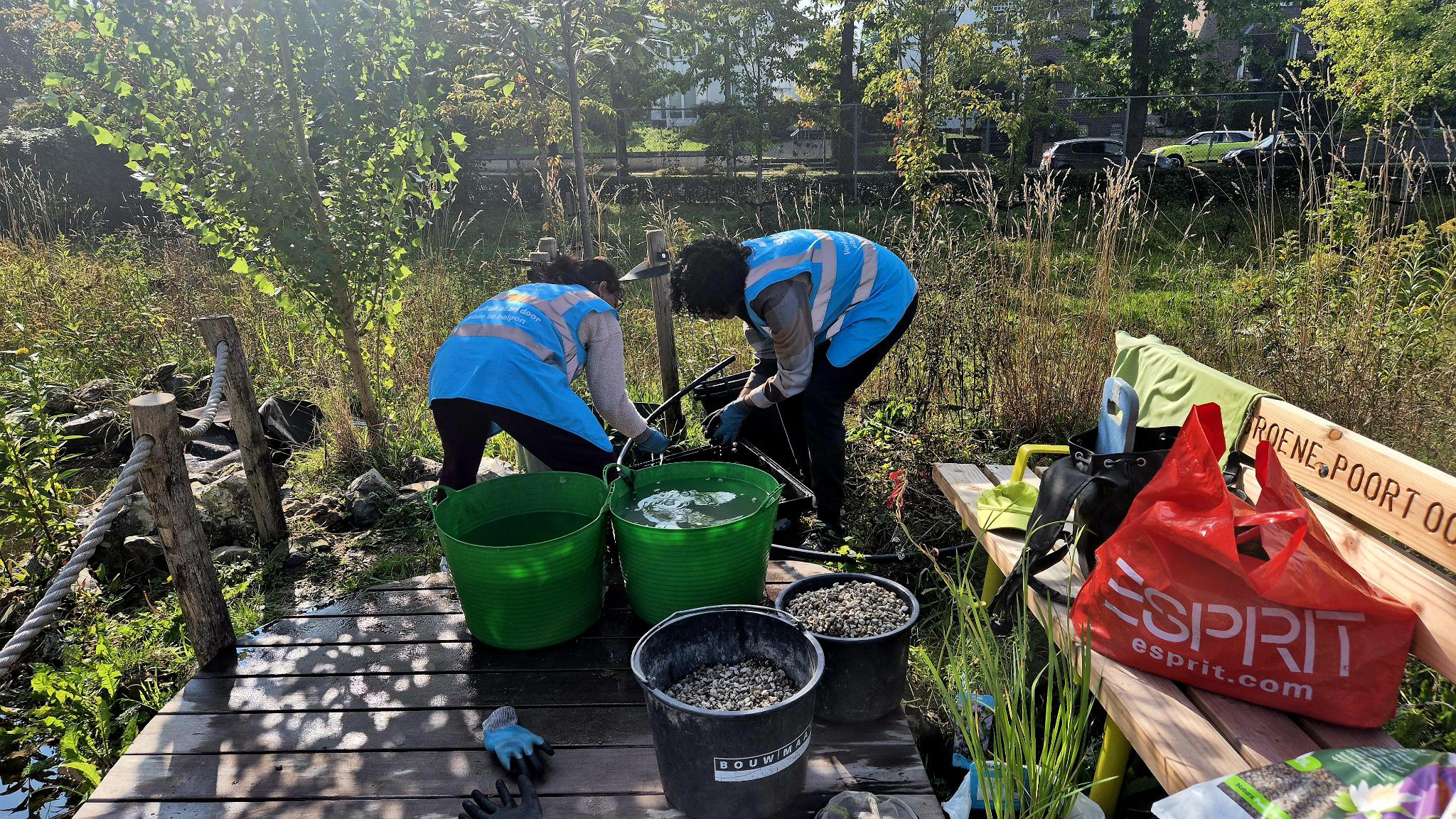 Twee klussers staan bij de waterpoel met bakken water, grind en nieuwe plantjes.