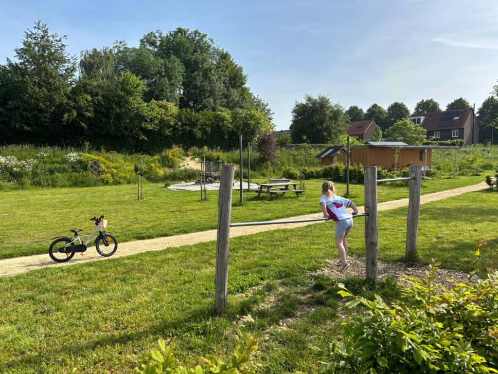Kind hangt over duikelrek. Op de achtergrond staat de waterspeelplek